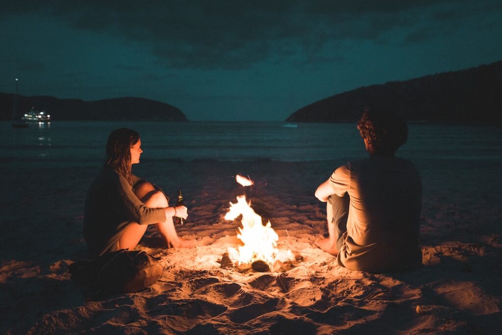 silhouetted-man-and-woman-sitting-by-a-beachside-bonfire