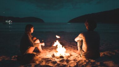 silhouetted-man-and-woman-sitting-by-a-beachside-bonfire